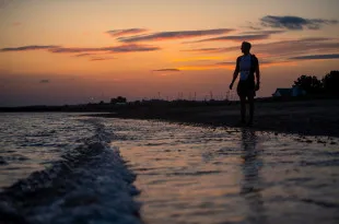 Man stood at coast with sunset behind him