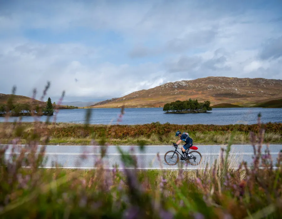 Participant cycling on road past water