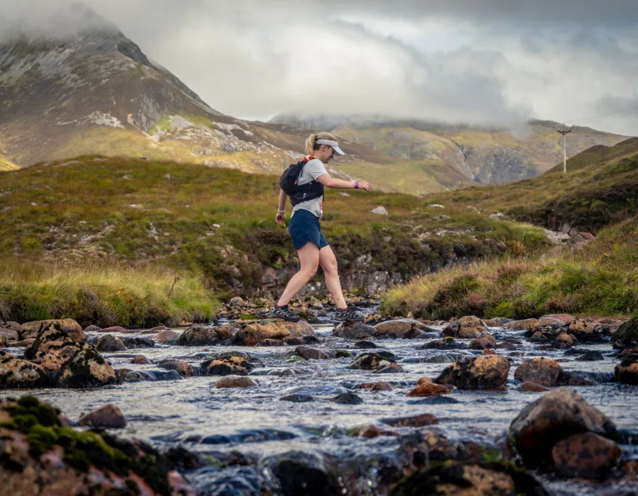 Woman crossing stream, surrounded by greenery