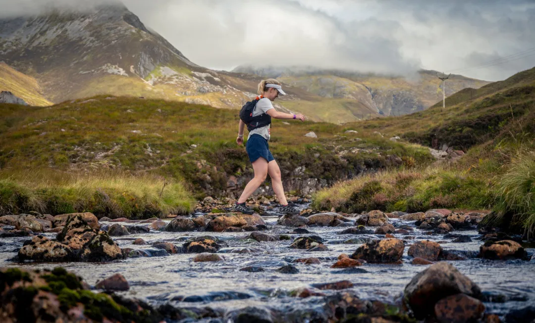 Woman crossing stream, surrounded by greenery
