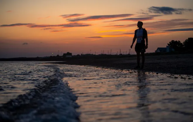 Man stood at coast with sunset behind him